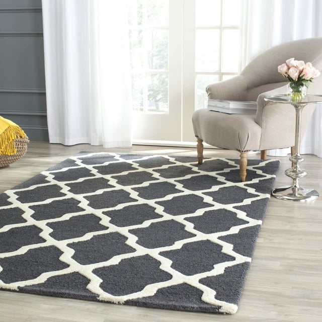 Safavieh Cambridge Liam Geometric Area Rug in charcoal and white with hand-tufted wool texture and geometric lattice pattern, placed on light hardwood flooring beside a beige armchair and silver side table with pink roses, ideal for adding modern American style to home or office.