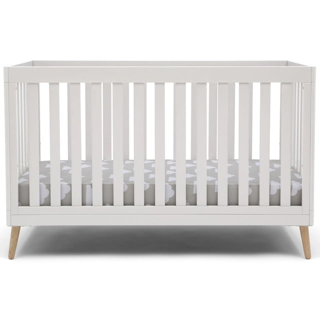 Delta Children Lit de Bébé 4-en-1 Convertible en Blanc avec Pattes Évasées en Bois Naturel, Lattes Verticales et Matelas Gris à Motif de Nuages Blancs, avec Hauteur de Matelas Ajustable et design Convertible en Lit pour Tout-Petit, Lit de Jour Ou sofa.