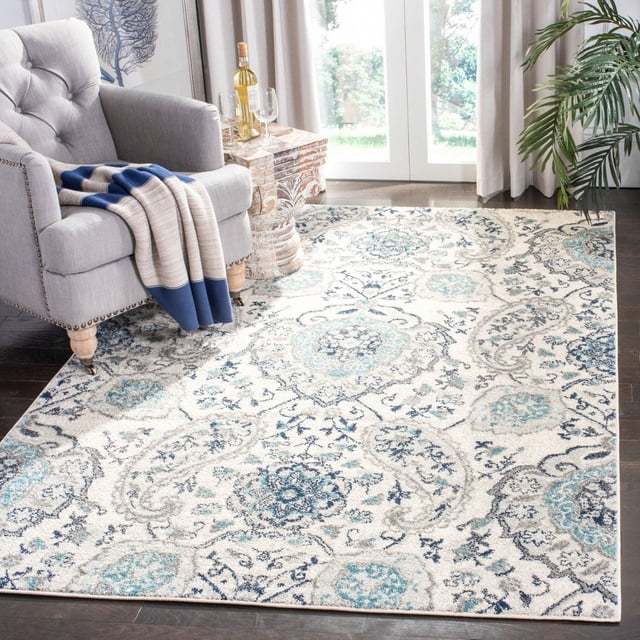 SAFAVIEH Madison Heather Floral Paisley Area Rug with a power-loomed floral paisley pattern in blue, teal, and grey on cream, placed on dark hardwood flooring beside a grey armchair with a blue and beige striped throw, suitable for transitional and contemporary home decor.
