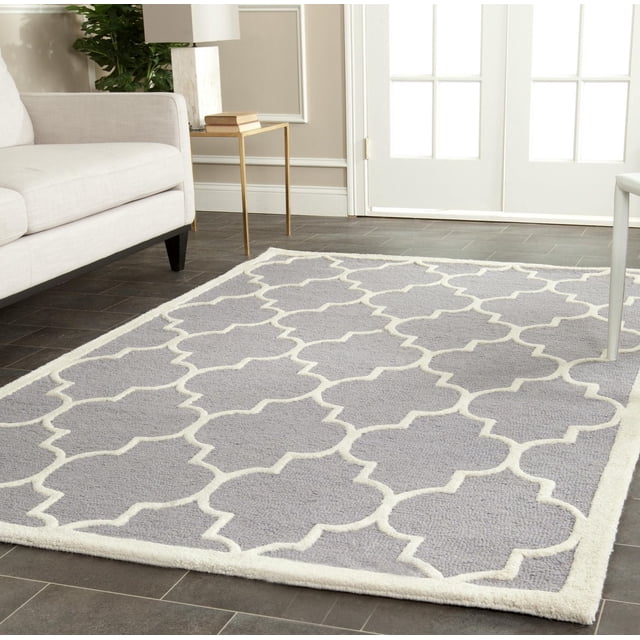 Safavieh Cambridge Kevin Geometric Area Rug featuring hand-tufted wool with a grey base and white geometric trellis pattern, displayed on dark tile flooring in a living room with a beige sofa, gold side table, and white French doors, ideal for adding modern American style and texture to home or office decor.