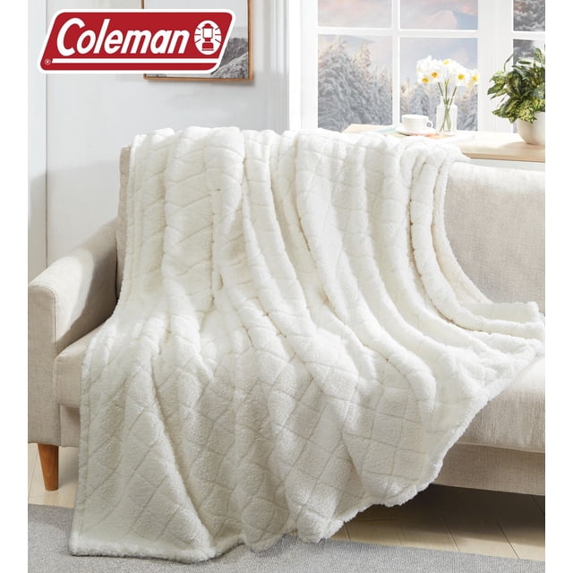 Coleman Couverture Sherpa Surdimensionnée Certifiée en Blanc avec Motif Matelassé à Losanges, Drapée sur un sofa beige dans une Pièce Lumineuse avec des Arbres Enneigés visible à Travers la Fenêtre, Fabriquée en Sherpa Brossé Double Face pour une Chaleur et une Douceur Toute l'Année, Convient Aussi pour Se Douiller Lors de Soirées Fraîches.