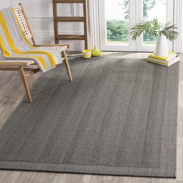 SAFAVIEH Palm Beach Candyce Solid Geometric Area Rug in rectangular shape with durable gray sisal fibers and subtle oscillating striped geometric patterns, placed on light wood flooring in a bright room with a wooden chair draped in a yellow and gray striped throw, a wooden ladder shelf, and a white vase with palm leaves on stacked books near glass doors, ideal for casual-coastal or urban living spaces.
