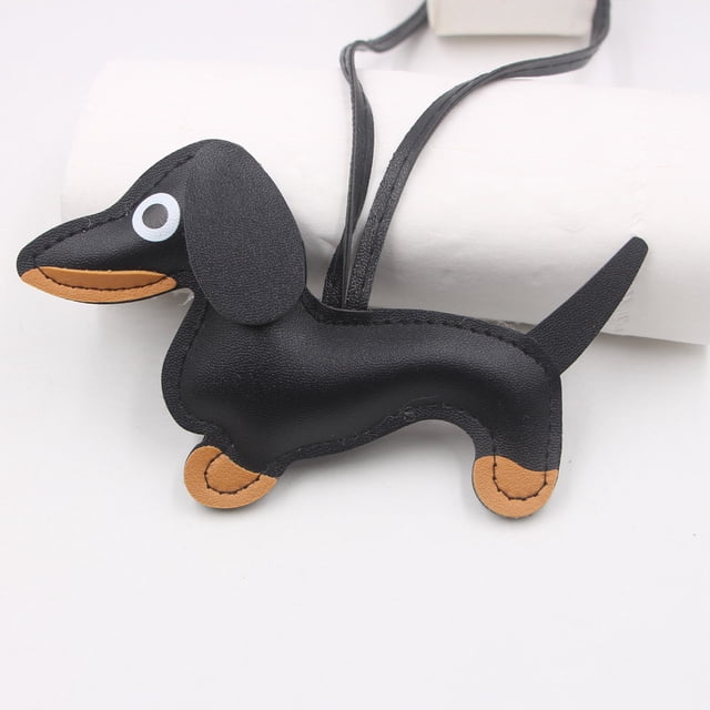 Leather Dachshund Keychain with Rope Handmade Sausage Dog Bag Charm for Phone Case, Car Keys & Pet Lover Accessory. The keychain features a black leather dachshund shape with tan accents on the paws and snout, showcasing hand-sewn craftsmanship. It includes a long leather strap for versatile use, such as attaching to keys, backpacks, or handbags. This playful and practical accessory is ideal for pet lovers and serves as a conversation piece.