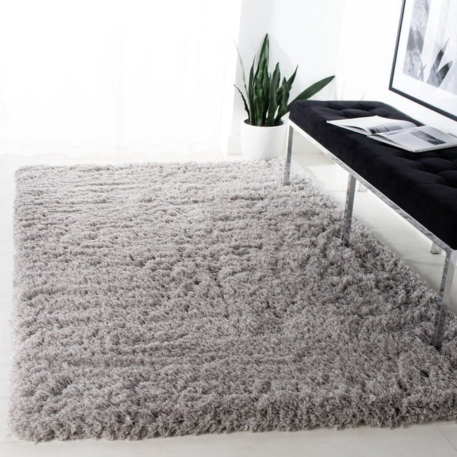 SAFAVIEH Polar Abbot Tapis Shag en Peluche Extrême Uni Gris Pâle avec une pile Pelucheuse de 3 Pouces d'Épaisseur, Posé sur un Plancher Clair à Côté d'Un Banc Capitonné Noir avec des Pattes Chromées et une Plante Serpent en Pot, Mettant en Valeur Sa texture Douce et Son Usage comme Tapis d'Accent Moderne.