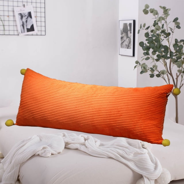 HOARBOEG Extra Long Pillows Cool Body Pillows for Bed Sofa Shredded Memory Foam Full Pillows Pillowcase and Pillow Core with Zipper, Orange 23.62in. This decorative body pillow features a vibrant orange ribbed texture with green pom-poms at each corner, adding a stylish touch. Made from 95% polyester and 5% spandex, it provides a soft, breathable surface for lounging or sleeping. Positioned on a white sofa with a cozy blanket, the minimalist room includes a plant and framed artwork in the background.