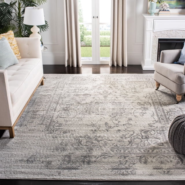 Safavieh Adirondack Zoey Tapis Traditionnel Délavé Mettant en Vedette un Motif floral Abstrait Gris et beige Atténué avec un Style Vieilli Surteint, Fabriqué à Partir de Fils de Polypropylène Durables, Posé sur des Planchers de Bois Franc Sombres dans un Salon avec Sièges Rembourrés Crème et beige, un Foyer Blanc et des Portes-Fenêtres avec des Rideaux beige.