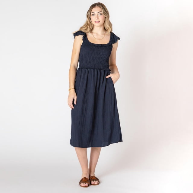 Devoted Robe midi Sans Manches à Volants aux Épaules en Bleu Marine, avec un Corsage Smocké Qui Épouse la Taille et une Jupe Évasée Fluide, Exposée sur un Modèle Debout Face à l'Avant sur Fond Blanc, Assortie à des Sandales Brunes et à de Simples Bijoux Dorés, Convient aux occasions de cocktail et de Fête.