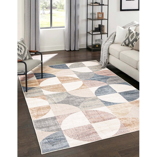 ECARPET Bennett Contemporary/Modern Area Rug with abstract geometric patterns in beige, blue, gray, and brown tones, placed on dark hardwood floor in a living room featuring a beige sofa with patterned cushions, a patterned accent chair, and a black metal shelving unit near a window with gray curtains, suitable as an accent rug adding soft texture to living spaces.