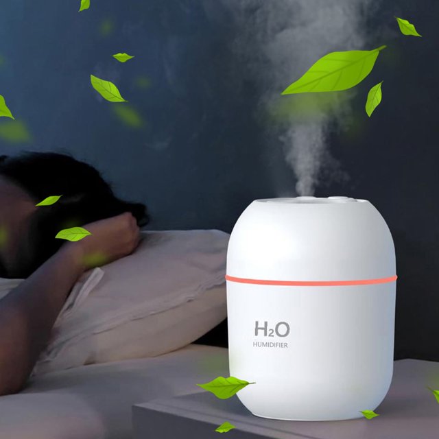 Dvkptbk Humidifier, a USB rechargeable portable humidifier in white with a compact design measuring 9.5x7.6x7.6cm. Features include a 220ml water tank, multiple spray modes, a hydration meter, and a colour gradient night light. Ideal for home, office, bedroom, or travel use. Shown emitting mist on a bedside table with green leaves in the foreground.