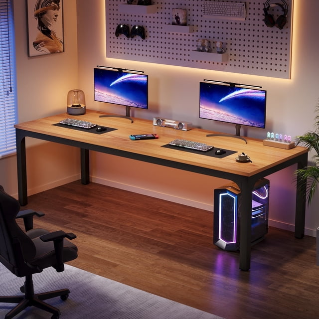 Fnova 78.7" Modern Computer Desk with wood desktop and metal frame in light brown. The desk features a spacious 78.74" x 27.56" surface accommodating two computers, ideal for dual-person work, multitasking, or gaming. It has a 0.59" thick wood-grain desktop, 1.97" x 1.97" metal legs, and an upgraded support frame for enhanced stability. Adjustable protective foot caps prevent floor scratches and ensure stability on uneven surfaces. Shown in a modern home office setup with dual monitors, a gaming chair, and accessories.