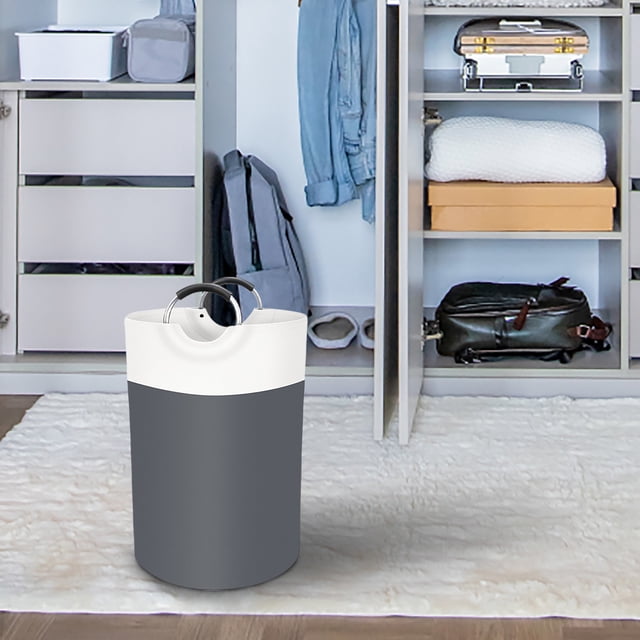 Clearance Tyidzon Laundry Basket Laundry Hamper, collapsible and freestanding with foam-protected aluminum handles, shown in a modern bedroom setting. The basket features a tall, two-tone design with a grey base and white top, offering an 82L capacity for storing clothes, toys, or other items. Suitable for laundry room storage, college dorms, or family use, and designed for space-saving organization.