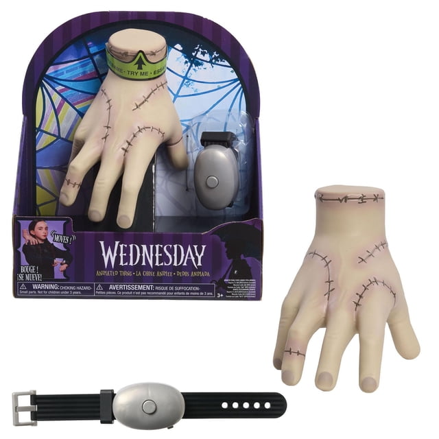 Wednesday Animated Thing, 3+, interactive pale disembodied hand toy with stitched details, includes shoulder strap base and wristband remote control for finger movements, shown in purple packaging with stained glass window design, suitable as a Halloween costume accessory for children aged 3 and up.