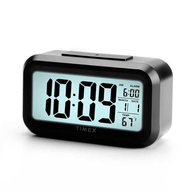 Portable Battery Operated Alarm Clock with Large Display featuring a 1.5-inch white backlit LCD showing 10:09 AM, alarm set for 6:00, calendar date January 1, and temperature 67°F in a black rectangular case with rounded corners and Timex logo, suitable for travel or bedside use.