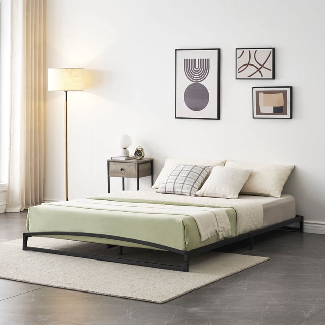 Cadre de Lit Bas Format Simple, Cadre de Lit Plateforme en Métal Robuste de 6 Pouces en Noir avec Fini Enduit de Poudre. le Cadre Présente un design Arqué unique à la Tête et aux Pieds pour Empêcher le Matelas de Glisser. Il Est Profil Bas, Se Tient à 6 Pouces du Sol, Convient aux Matelas Plus Grands Ou aux Familles avec Enfants et Animaux de Compagnie. la construction en Métal Robuste Supporte jusqu'à 1000 Livres et Comprend des Bandes de Mousse Silencieuses Sans Bruit. Présenté dans un Cadre de Chambre Moderne avec un Tapis beige, une table d'Appoint et une Oeuvre