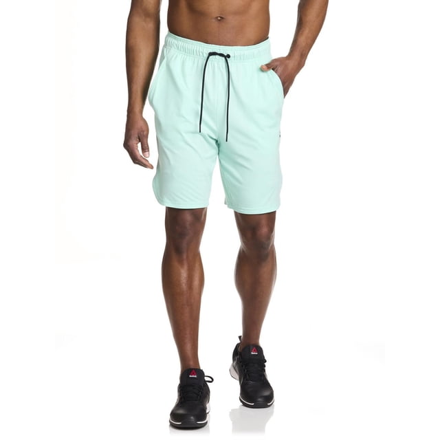 Reebok Shorts Delta Core pour Hommes en Vert Menthe Pâle avec Taille Élastique, Cordon de Serrage Noir, Poches Latérales et logo Reebok Delta sur le Côté, Portés par un Modèle Masculin Debout Orienté vers l'Avant, Assortis aux Chaussures Athlétiques Reebok Noires, Idéales pour l'Entraînement Ou les Tenues Décontractées.