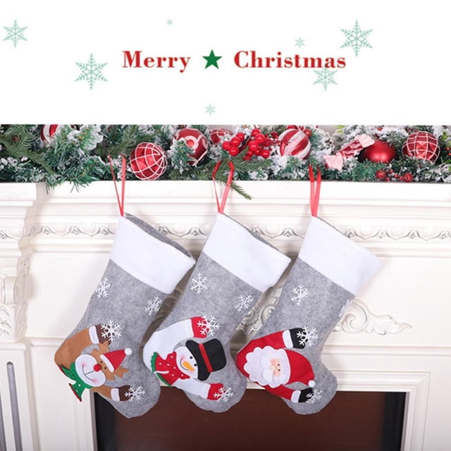 Christmas Stockings Socks With Lights Bright Christmas Stockings hung on a white fireplace mantel. The three gray stockings feature festive designs, including a reindeer, snowman, and Santa Claus, with snowflake patterns. Made of non-woven fabric, they are ideal for Christmas tree decorations or family holiday decor. Above the mantel, a garland with red ornaments and berries enhances the festive atmosphere.