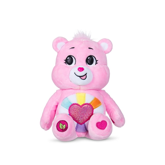 Care Bears Fun Size Sparkle Plush (Eco) - Hopeful Heart Bear, a 9-inch pink plush bear with a glittery heart and rainbow rays belly badge, made from soft sustainable materials, featuring embroidered heart and leaf symbols on feet, front-facing on white background, ideal for cuddling and collecting.