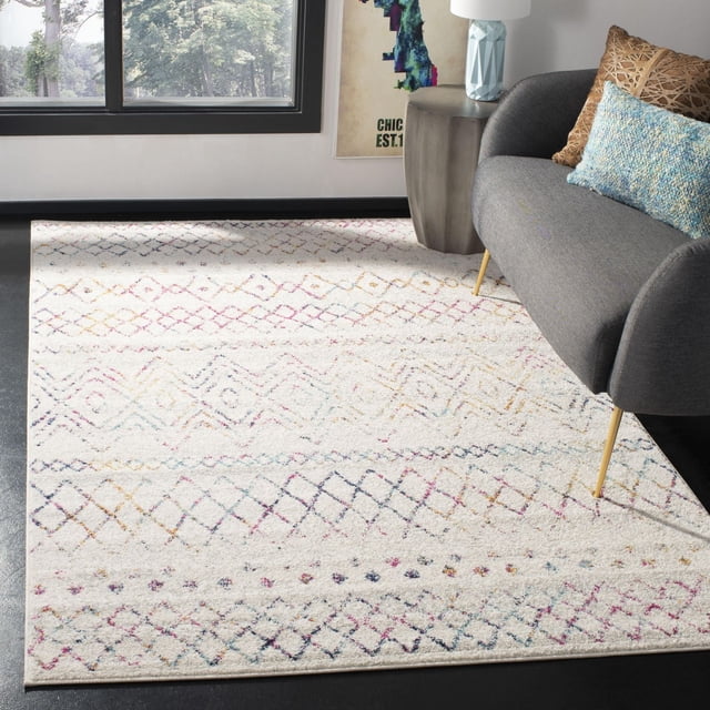 Safavieh Madison Hannah Geometric Area Rug with a cream base and multicolored diamond and zigzag patterns, placed on a dark floor in a modern living room featuring a gray sofa with blue and brown cushions and a concrete side table near a large window with a view of trees, ideal for adding durable transitional style to home decor.