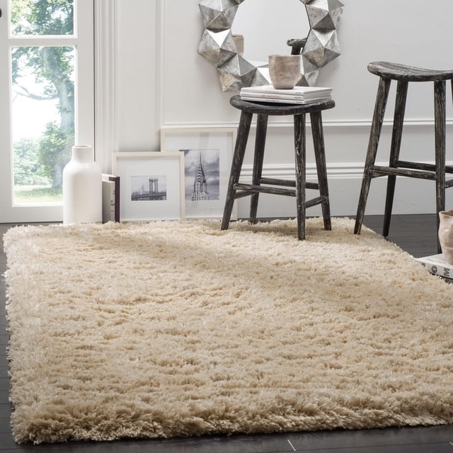 SAFAVIEH Polar Abbot Tapis Shag en Peluche Extrême Uni beige avec une pile de Peluche de 3 Pouces d'Épaisseur, Posé sur un Plancher de Bois Franc Foncé dans une Pièce Lumineuse Comprenant Deux Tabourets en Bois Noir Vieilli, un Miroir Mural Géométrique Argenté et des photos Encadrées de Paysage Urbain Noir et Blanc, Idéal pour Ajouter Chaleur et texture aux Intérieurs de la Maison.
