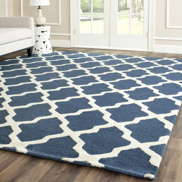 Safavieh Cambridge Liam Geometric Area Rug in navy blue with white geometric lattice pattern, hand-tufted wool texture, displayed on hardwood floor in a bright room with white walls and glass doors, ideal for modern home or office decor.