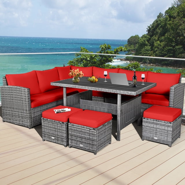 Gymax Ensemble de Conversation Sectionnel de Patio en Rotin 7 Pcs avec Coussins Rouges, Doté d'Un Cadre en Rotin Gris Mixte. Comprend 3 Chaises d'Angle, 3 ottomans et une table Rectangulaire avec Dessus en Bois Plastique à Lattes. Conçu pour une Utilisation Extérieure, l'Ensemble Est Disposé sur un Patio Surplombant une Vue Océanique Pittoresque. les Coussins Sont Épais et Rembourrés d'Éponge pour le Confort, et la table Est Stylée avec des Articles Décoratifs comme des Fleurs et des Verres à Vin.