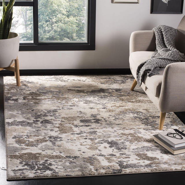 SAFAVIEH Spirit Mira Abstract Camouflage Area Rug with plush cut pile and earthy beige, taupe, and gray abstract camouflage pattern, placed under a beige accent sofa with wooden legs and gray knitted throw near a large window with green trees and a potted plant. Suitable as an accent rug to add organic texture and warmth to room decor.