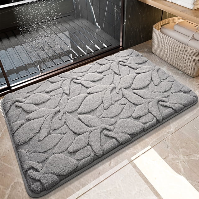 Staron Bath Mats for Bathroom, a 24x16-inch gray microfiber bathroom rug with a soft, absorbent texture and a non-slip backing. The mat features a decorative leaf pattern and is placed on a tiled bathroom floor near a shower area. Designed for quick drying and machine washability, it is suitable for use in bathrooms, bedrooms, or as an entrance mat.