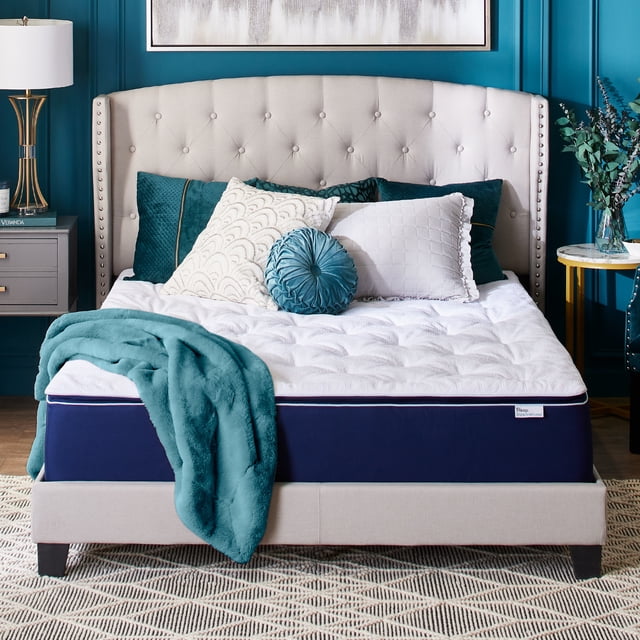 Sleep Innovations Skyler Gel Memory Foam Mattress, Full, 12-inch, Plush Pillow Top displayed in a modern bedroom setting. The mattress features a white quilted pillow top with a navy blue base, placed on a beige upholstered bed frame with a tufted headboard. Decorative pillows and a teal throw blanket accent the bed, complementing the teal wall and gold-accented decor. Designed with gel memory foam for cooling and pressure relief, this mattress offers plush support for all sleep positions.