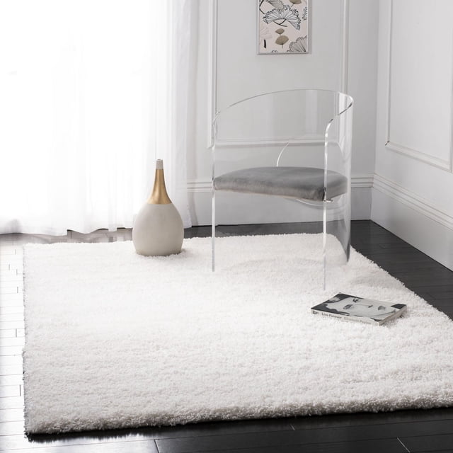 Safavieh California Tapis Shag Uni en Peluche Blanc avec un Empilage de Polypropylène super dense de 4,5 Kg/m2, Présenté sur un Plancher de Bois Franc Foncé avec une Chaise en Acrylique Transparent avec Coussin Gris, un vase Décoratif avec accent Doré et un Livre, Idéal pour Ajouter une texture Peluche et du Confort aux Espaces Domestiques Modernes.