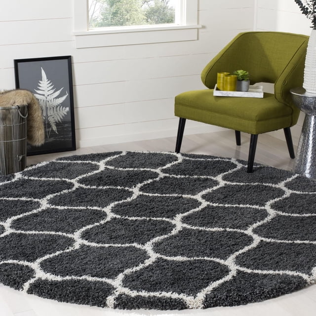 Safavieh Hudson Arline Geometric Shag Area Rug featuring a thick plush dark gray shag pile with white onion-shaped tile patterns in a round shape on light hardwood flooring, styled beside a green modern accent chair and decorative items, ideal for adding texture to contemporary living rooms.