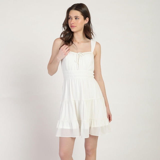 Bloom Girl Robe en Popeline, Tailles TP-TG, Robe Courte Blanche Sans Manches avec Corsage Ajusté, Taille Froncée et Jupe Fluide à Volants en Tissu polyester Doux, Montrée Orientée vers l'Avant sur un Modèle sur un Fond Uni, Idéale pour le Quotidien et Souvent Utilisée comme Couche Légère à Enfiler sous la lingerie.