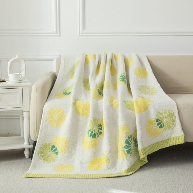 Mainstays Jeté Douillet Citron 50 Po x 60 Po Drapé sur un sofa beige, Présentant une texture Pelucheuse avec un Fond Blanc et des Imprimés de Citron Jaune et de Feuilles Vertes, Bordé d'Une Bordure Vert Pâle. Utilisé Souvent comme Couverture Jetée pour la Chaleur et le décor.