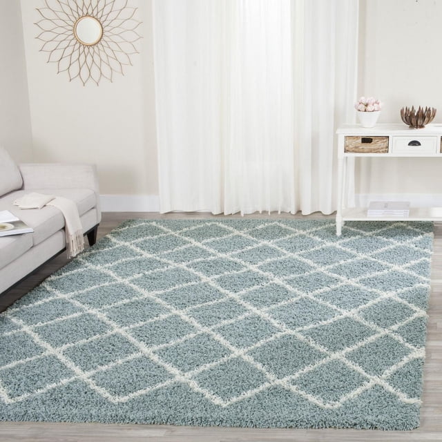 Safavieh Dallas Jerrie Geometric Shag Area Rug with plush blue synthetic fibers and white diamond pattern, displayed on light wood flooring in a modern living room beside a grey sofa and white console table, suitable for high-traffic areas and adding soft texture to contemporary decor.