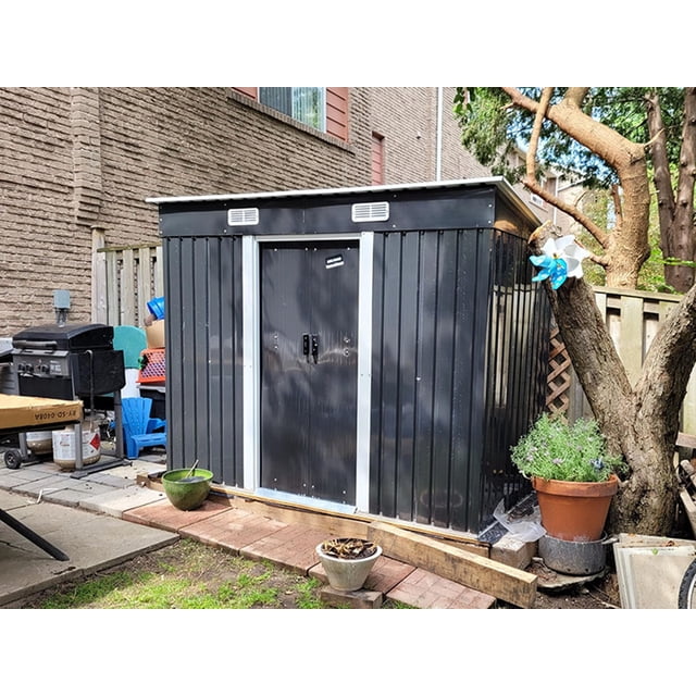 Relyard 4x8 Rangement Extérieur en Métal pour Jardin Shed en Acier Galvanisé avec une surface Enduite de Poudre pour la Résistance à la Rouille et à la corrosion. le Shed Présente des Portes Coulissantes pour un Accès Facile, des Évents d'Air Intégrés pour une Meilleure circulation d'Air, et un Toit en Pente pour un Ruissellement Efficace de l'Eau et une Prévention de la Neige. Montré dans un Cadre de Cour Arrière avec des Plantes Environnantes et de l'Équipement Extérieur.