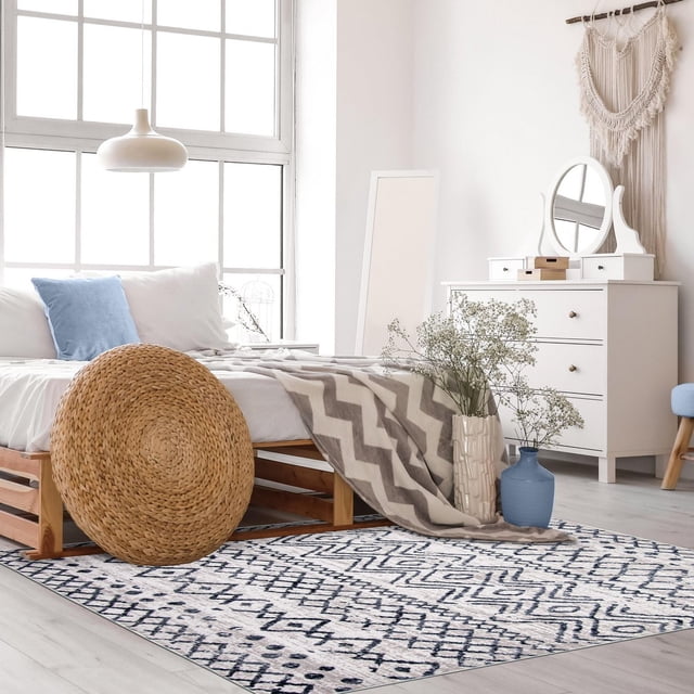 Ecarpet Tapis d'Intérieur Géométrique Collection Astrid avec Motif Géométrique Bleu Marine et Blanc sur Polypropylène Résistant aux Taches, Placé dans une Chambre Éclatante avec Plancher de Bois Clair, Cadre de Lit en Bois avec Coussins Blancs et Bleus, Jeté à Chevrons, Commode Blanche avec Miroir et vases Décoratifs avec Fleurs, Idéal pour les Zones Intérieures Très Passantes.