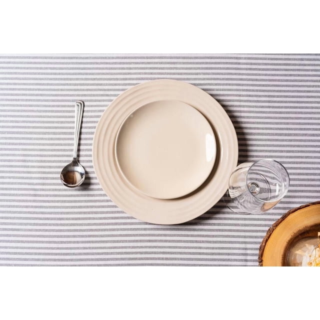 Fabstyles 100% Cotton Bistro Stripe Table Cloth in grey with horizontal stripes, displayed with stacked beige ceramic plates at center, a metal spoon to the left, a clear glass to the right, and a wooden bowl edge visible at bottom right, suitable for indoor and outdoor dining use.
