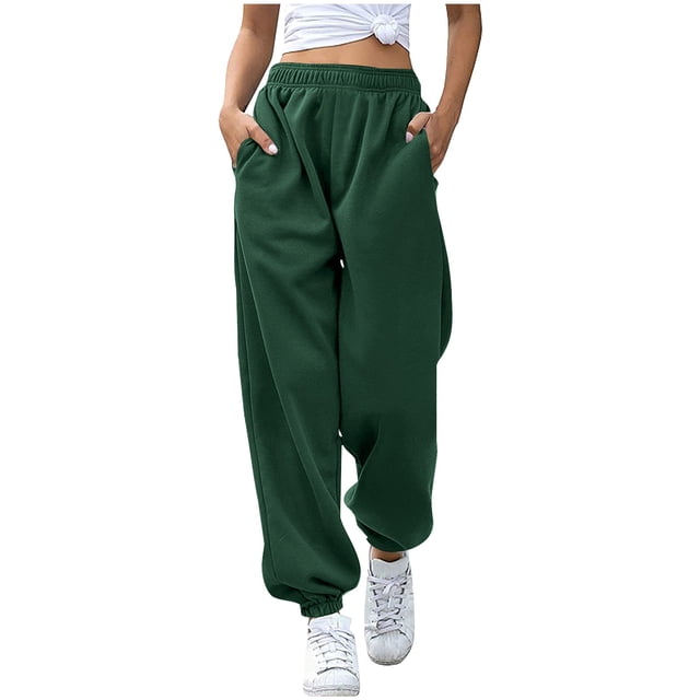 Timegard Sweatpants for Women Joggers Elastic Waist Drawstring Fall Winter Casual Comfy Pants with Pockets in a dark green color. These sweatpants feature a relaxed fit with an elastic waistband and drawstring for adjustable comfort. Made from 95% polyester and 5% spandex, they are soft, breathable, and lightweight. The design includes two side pockets and elasticized cuffs, making them suitable for lounging or casual outings. Shown paired with white sneakers and a knotted white top.
