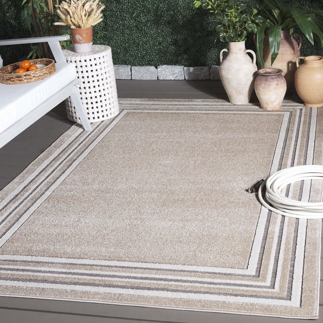 SAFAVIEH Cabana Rado Bordered Indoor/Outdoor Area Rug in beige with bordered geometric stripes, made of durable synthetic yarns resistant to weather, wear, mold, and sun fading, placed on a gray deck floor with white wicker side table, white bench with basket of oranges, and ceramic vases with plants, suitable for busy indoor or outdoor areas.