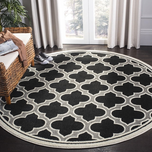 Safavieh Amherst Wilson Tapis Géométrique pour Aire, Rond avec Motif de Treillis Géométrique Noir et Gris et Bordure Gris Pâle, Polypropylène Tissé Mécaniquement pour la Durabilité dans les Espaces Intérieurs Ou Extérieurs à Fort Achalandage, Montré sur Plancher de Bois Franc Foncé à Côté d'Une Chaise en Osier et des Espadrilles.