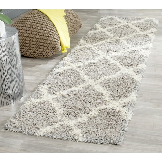 Safavieh Dallas Tapis Shag Géométrique Logan avec Motif de Carreaux Marocains Gris Pâle et Ivoire et Poil Shag en Polypropylène Doux, Exposé sur un Plancher de Bois Clair à Côté d'Un pouf Tricoté beige et d'Une table d'Appoint à Texture Argentée avec un Jeté Jaune, Convient pour Ajouter une Touche de Confort et de style à l'Intérieur de la Maison.