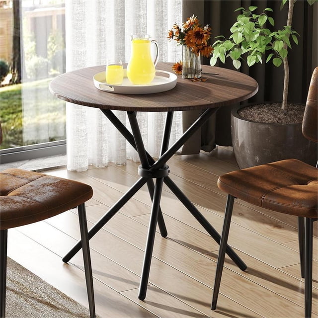 Homy Casa 31.5 inch Round Dining Table for two with an espresso MDF woodgrain top and black powder-coated metal base, shown in a bright kitchen nook with two brown cushioned chairs, a white tray holding a glass pitcher and glass of orange juice, and a vase of orange flowers, ideal for small kitchens or breakfast nooks.