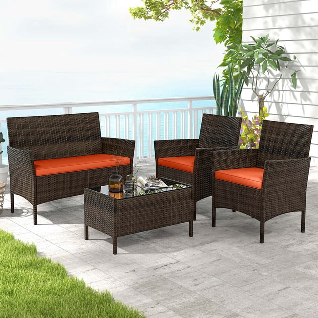 Costway 4 PCS Patio Furniture Set with Washable Cushions and Tempered Glass Coffee Table in orange. This 4-piece set includes a loveseat, two armless chairs, and a rectangular coffee table with a tempered glass top. The furniture is crafted from hand-woven mix brown PE rattan and supported by a durable metal frame, designed for outdoor use. The orange cushions are soft, thick, and feature removable covers for easy cleaning. The set is displayed on a patio with a view of the ocean, surrounded by greenery, showcasing its suitability for gardens, backyards, or poolside areas.