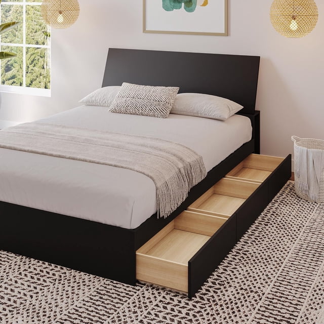 Nexera Corbo Storage Bed and Headboard in black melamine finish with three reversible storage drawers open on one side revealing light wood interiors, paired with a black headboard featuring lateral storage compartments, set in a modern bedroom with neutral bedding and woven pendant lights, suitable for storing bedding, clothes, and books.