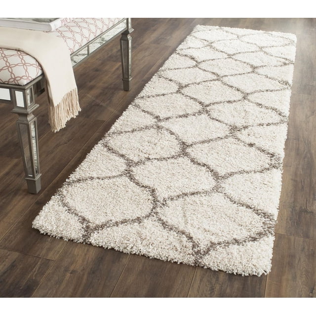 Safavieh Hudson Tapis Shag Géométrique Arline avec Poil Shag Épais Ivoire et Motifs de Carreaux en Forme d'Oignon Brun, Montré sur Plancher de Bois Franc Foncé à Côté d'Un Banc Miroir avec un Jeté beige, Convient pour Rehausser la texture dans les Espaces de Vie Modernes Ou Urbains.