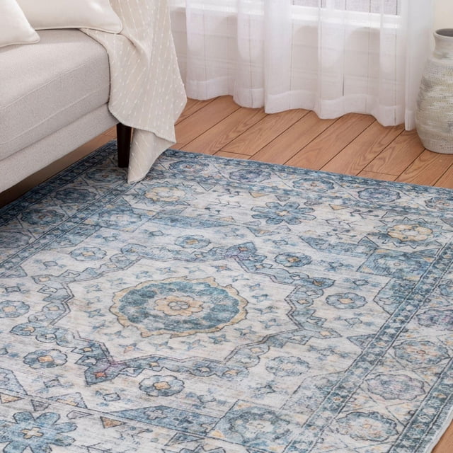 Tapis Tissé Banburry Bleu et Ivoire avec un Motif oriental Doux en Bleu Saphir, Ivoire et Jaune Subtil, Posé sur un Plancher de Bois Franc à Côté d'Un sofa beige et de Voilages Blancs, Fait de Fausse Fourrure 100 % polyester avec un Endos en Toile de Coton pour la Durabilité et la Douceur.