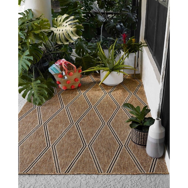 ECARPET Cypress Transitional Area Rug in tan and cream with woven geometric diamond patterns, placed on a textured outdoor floor near a white wall and black door. Styled with potted green plants including monstera and aloe, and a woven basket with red pom-poms holding folded towels. Suitable for versatile indoor or outdoor spaces like living rooms, bedrooms, or hallways.