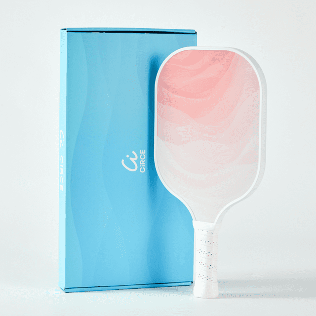 La Palette de Pickleball de Performance Cielo Couleur Blush par Circe Pickleball, Dotée d'Une surface en Fibre de Verre Renforcée G2P et d'Un Noyau en Nid d'Abeille Réactif pour une Puissance, un Contrôle et une Rotation Optimaux. la Palette Présente un design Texturé Rose et Blanc avec un Protège-Bord Blanc et une Poignée Ergonomique en Similicuir avec une Poignée Antidérapante Perforée. Elle Mesure 15,7 Pouces de Longueur, 7,9 Pouces de Largeur et Pèse 7,9 oz. la Palette Est Exposée à Côté de Son Emballage Bleu de Marque.