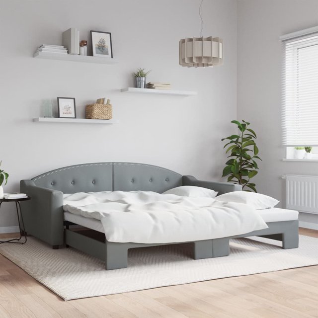 vidaXL Daybed with Trundle in dark grey fabric, measuring 100x190 cm, shown in a modern bedroom setting. The daybed features a tufted backrest, curved armrests, and a pull-out trundle for converting into a double bed. Made with a sturdy wooden and metal frame, it includes plywood slats for mattress support. The fabric is 100% polyester, offering a clean and breathable look. The room includes white shelves, potted plants, and natural light from a window.