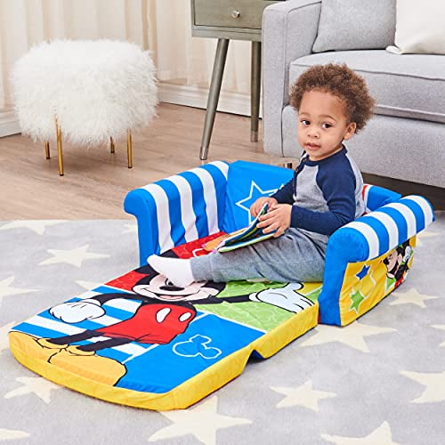 Marshmallow Furniture Canapé-Lit en Mousse 2-en-1 pour Enfants à Ouverture Rabattable Présentant un Thème Mickey Mouse vibrant. le Sofa Est Présenté dans un Décor de Salon avec un Enfant Assis Dessus, Tenant un Livre. le design en Mousse Léger Est Bleu avec des Graphiques Mickey Mouse Colorés et Se Retourne en Lit de 39 Pouces. Idéal pour les Tout-Petits de 2 Ans et Plus, Il Comprend une Housse en polyester Amovible, Lavable à la Machine avec une Fermeture Éclair de Sécurité. les Dimensions Sont 16 x 28,5 x 15 Pouces, Supporte jusqu'à 10