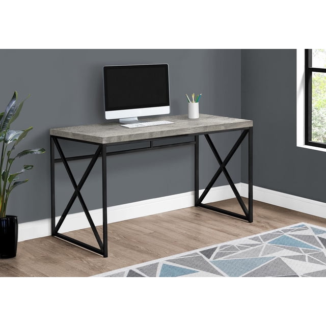Monarch Specialties Computer Desk with a thick grey reclaimed wood-look laminate top and black metal criss-cross legs, set in a modern home office with a desktop computer, pencil holder, and geometric rug on light wood flooring, also suitable as a versatile utility table.
